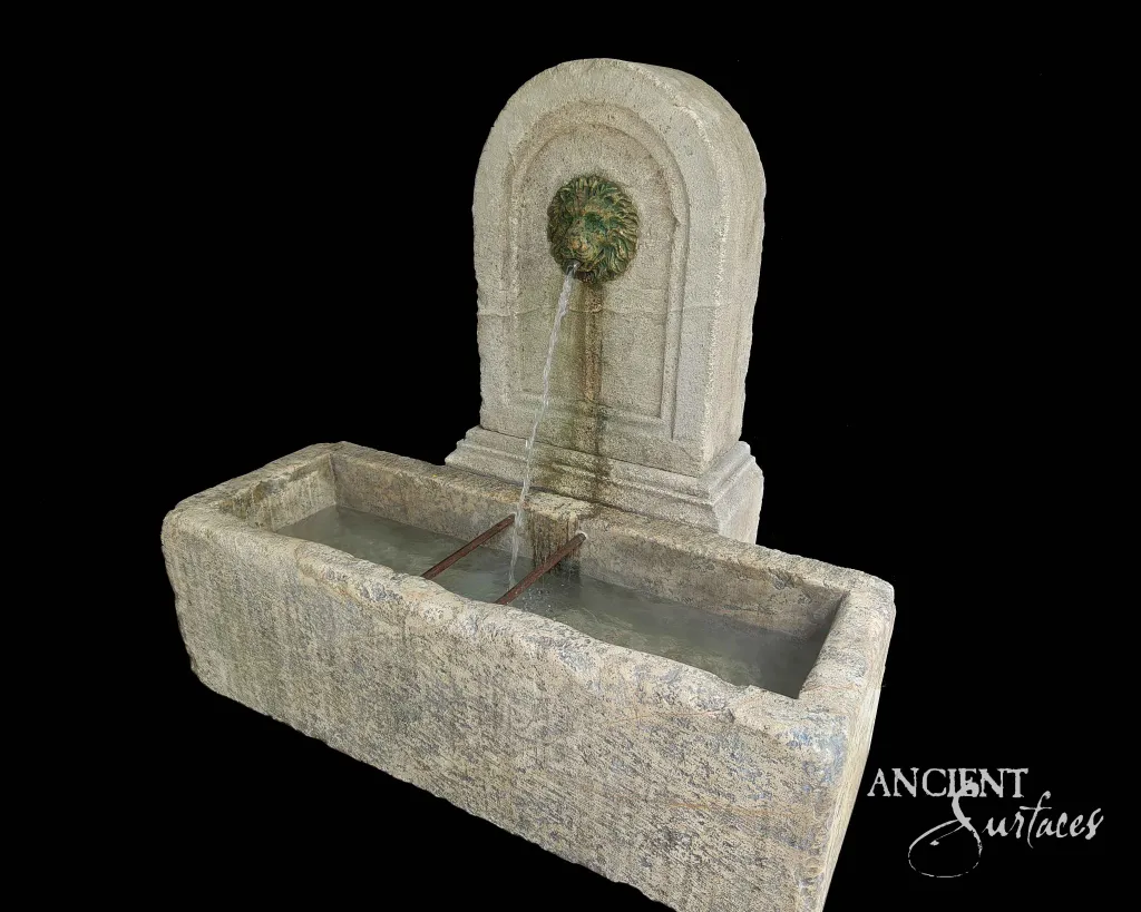 Antique reclaimed limestone wall fountain with a lion's-head spout flowing into a stone trough